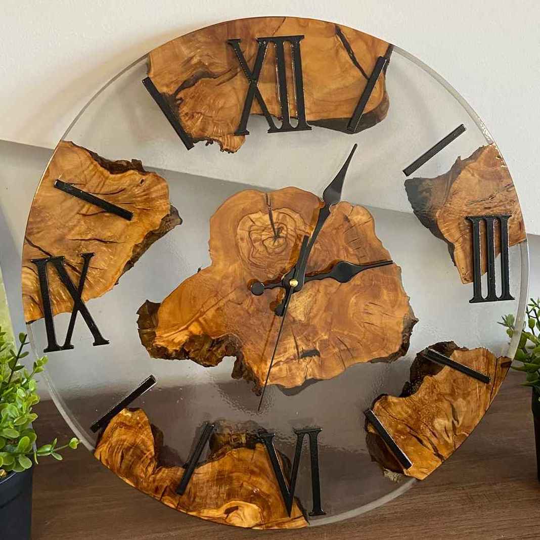 Primo piano di un orologio da parete artigianale in resina trasparente e radica di ulivo, con numeri romani neri, realizzato su misura da MM Wood&Resin Design a Roma. Il cliente può richiedere un preventivo gratuito chiamandoci o scrivendoci sul nostro sito.