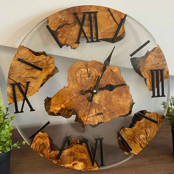 Primo piano di un orologio da parete artigianale in resina trasparente e radica di ulivo, con numeri romani neri, realizzato su misura da MM Wood&Resin Design a Roma. Il cliente può richiedere un preventivo gratuito chiamandoci o scrivendoci sul nostro sito.
