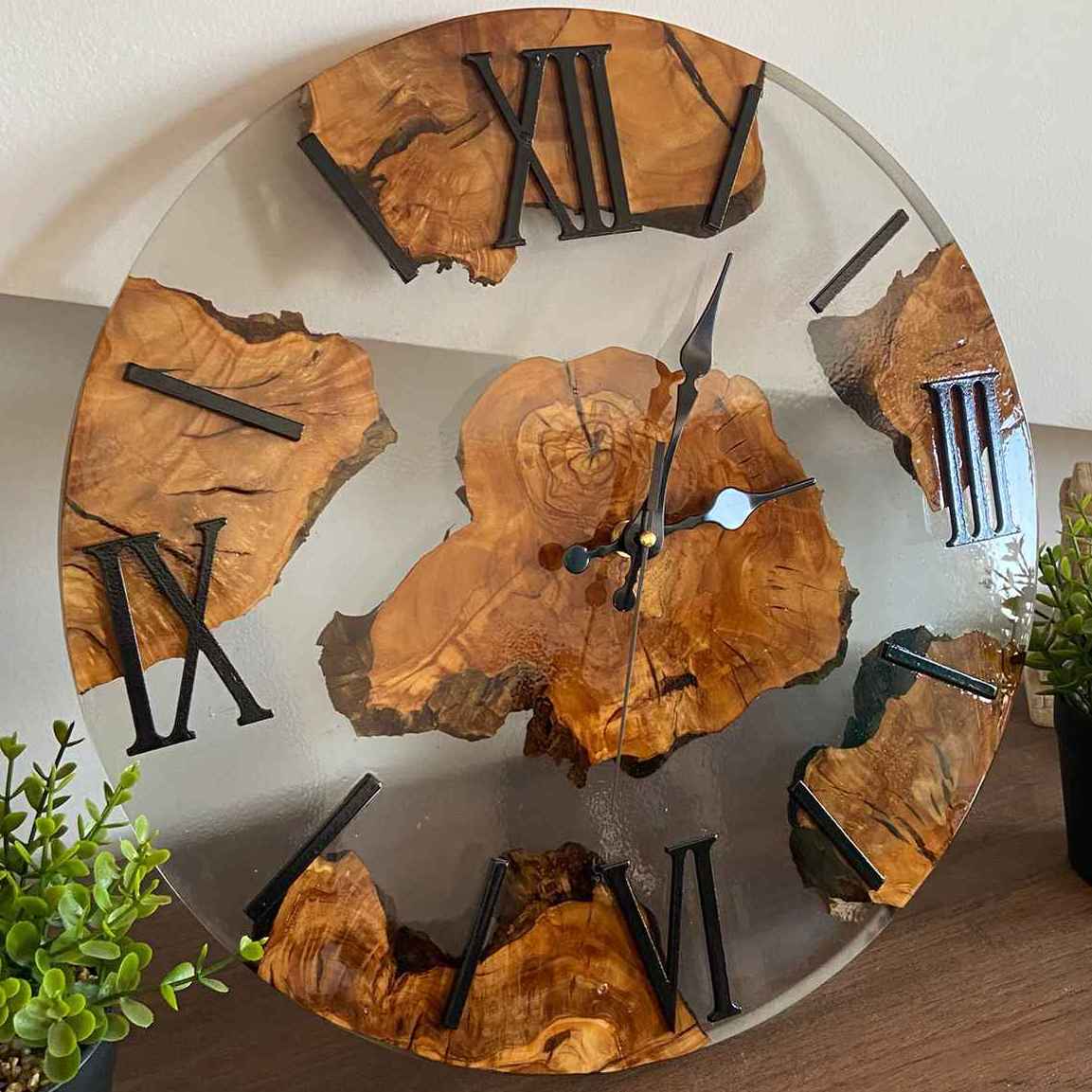 Primo piano ravvicinato di un orologio da parete artigianale in radica di ulivo e resina trasparente, con un focus sulle venature centrali del legno, le lancette decorate e i numeri romani.