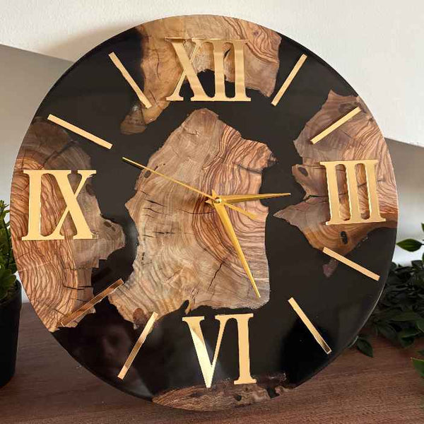 Primo piano di un lussuoso orologio da parete artigianale creato su misura a Roma, che combina il calore della radica di ulivo naturale con un'elegante base in resina epossidica nera lucida e luminosi numeri romani dorati.