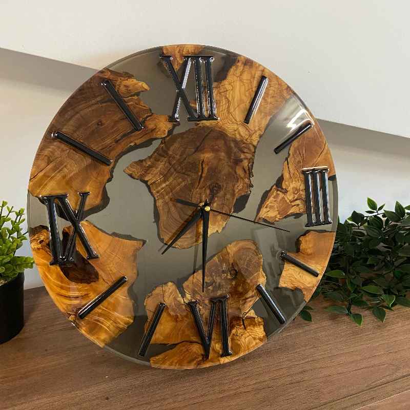 Esclusivo orologio da parete artigianale realizzato su misura a Roma, caratterizzato da sezioni di pregiata radica di ulivo inglobate in resina epossidica color grigio fumè traslucido, completato da eleganti numeri romani e lancette di colore nero.