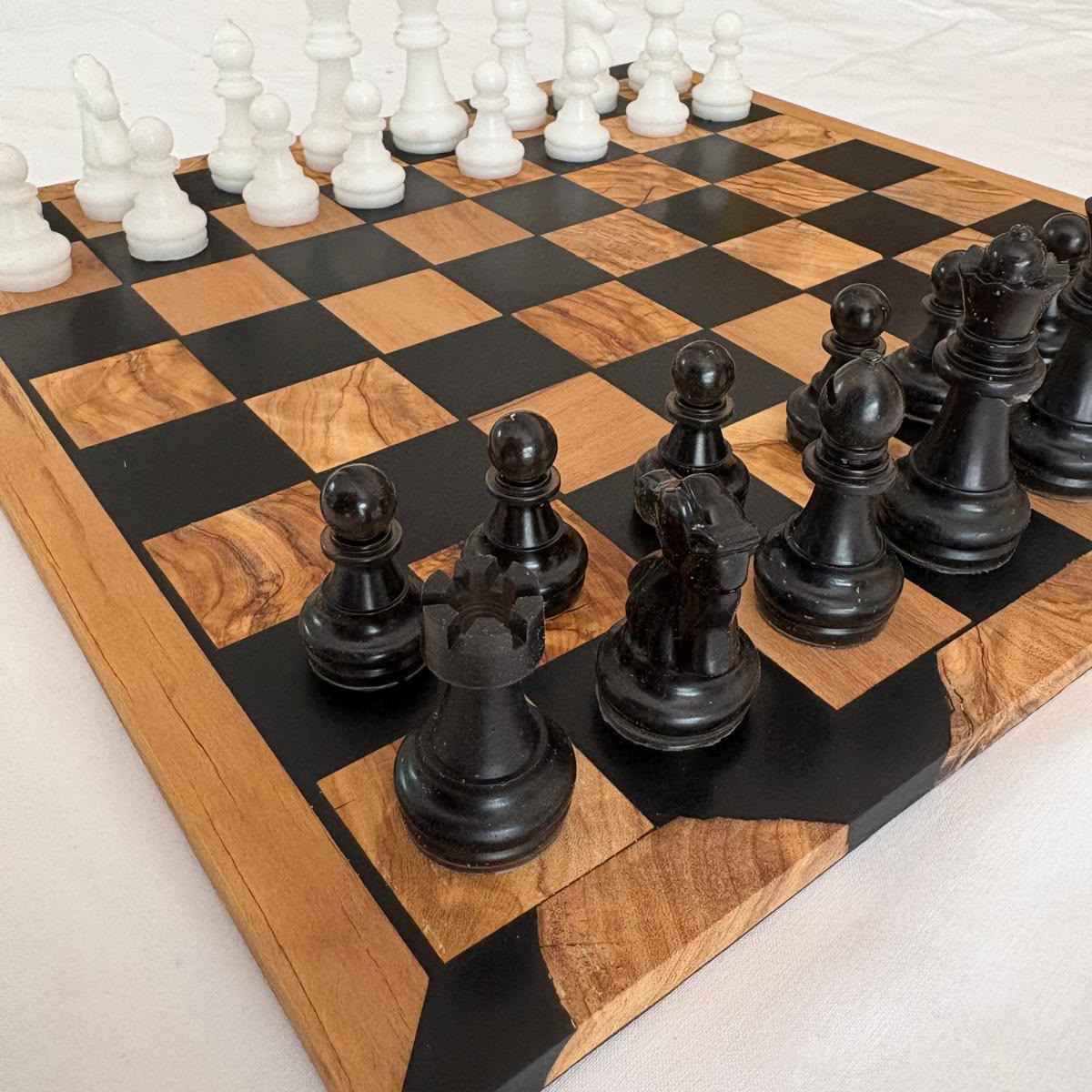Scacchiera artigianale realizzata in legno e resina nera, con pezzi degli scacchi posizionati per una partita in corso.