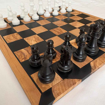 Scacchiera artigianale realizzata in legno e resina nera, con pezzi degli scacchi posizionati per una partita in corso.