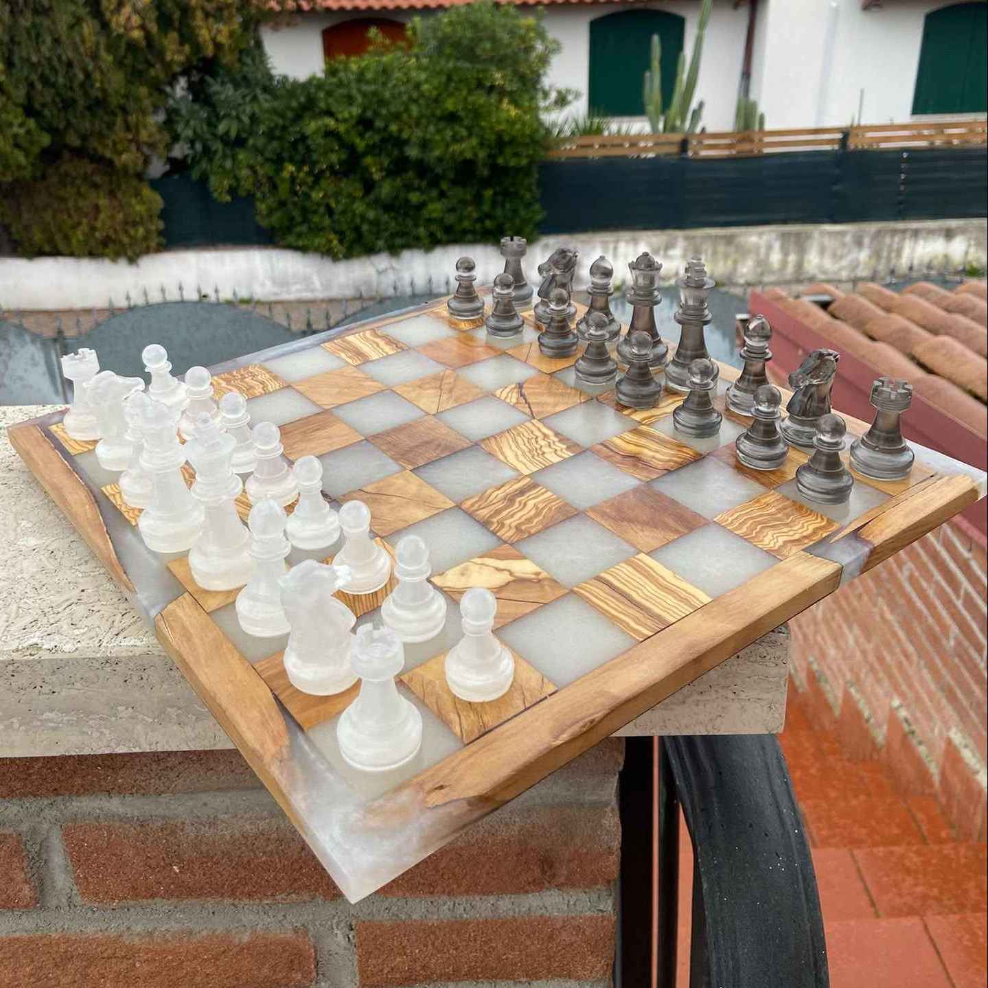 Scacchiera in legno e resina posizionata sul muretto in mattoni di un balcone, con i pezzi disposti sulla tavola. Ci troviamo a Roma e utilizziamo solo materiali di qualità. Perfetta per un regalo