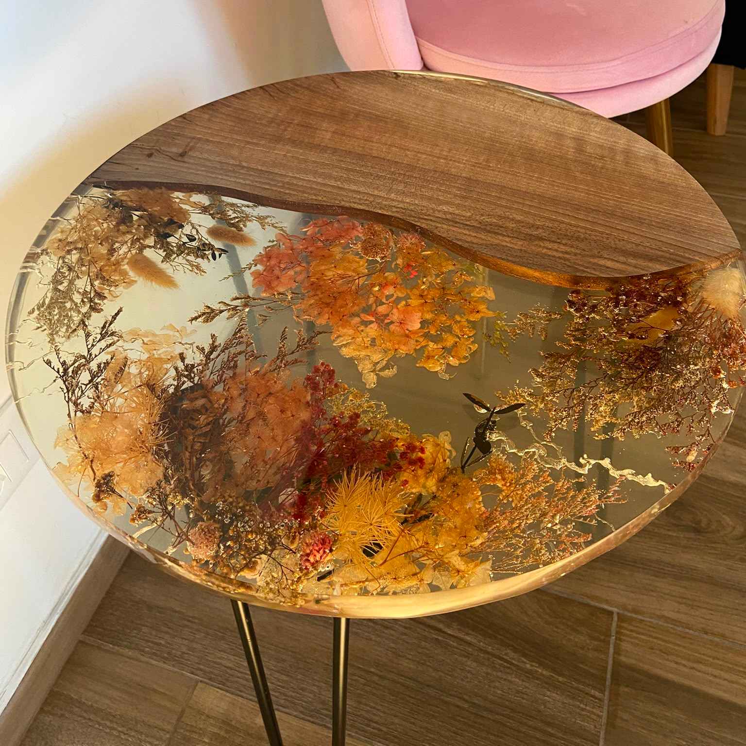 Dettaglio ravvicinato del piano di un tavolino da caffè rotondo, realizzato in legno di noce e resina trasparente con una ricca composizione di fiori essiccati.