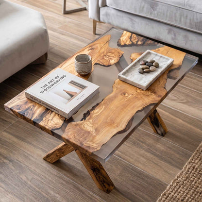Tavolino da salotto di design realizzato in legno di ulivo e resina trasparente, arredato con un libro e un vassoio decorativo, ambientato in un soggiorno elegante. Realizzato su misura a Roma da Marco morrone Wood and Resin Design