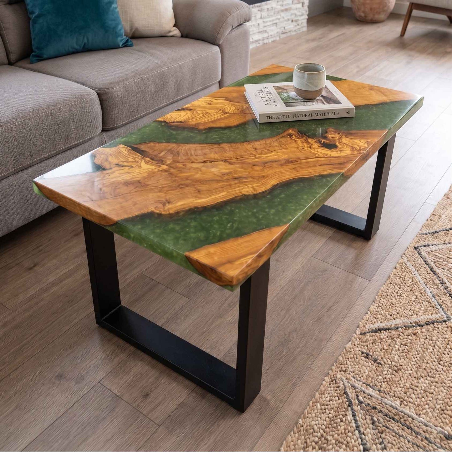 Tavolino da salotto in stile river table, realizzato artigianalmente in legno di noce e resina epossidica verde, posizionato su un pavimento in legno davanti a un divano.
