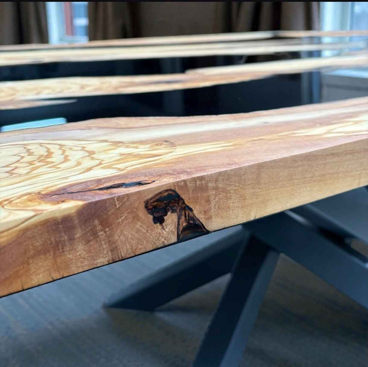 Dettaglio del bordo e delle venature naturali in legno massello di ulivo con colata di resina epossidica e basamento in metallo nero per tavolo da pranzo.