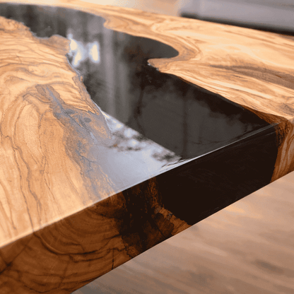 Primo piano dell'angolo e dello spessore di un tavolo in legno di ulivo con fiume centrale in resina epossidica nera e finitura lucida.
